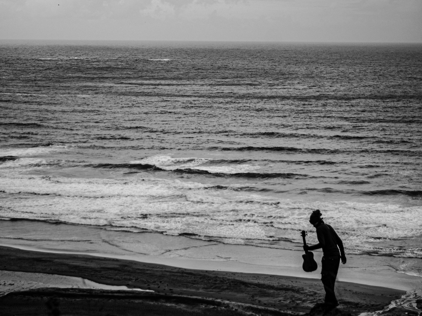 Un musicien, guitare à la main, sur la plage face à la mer.