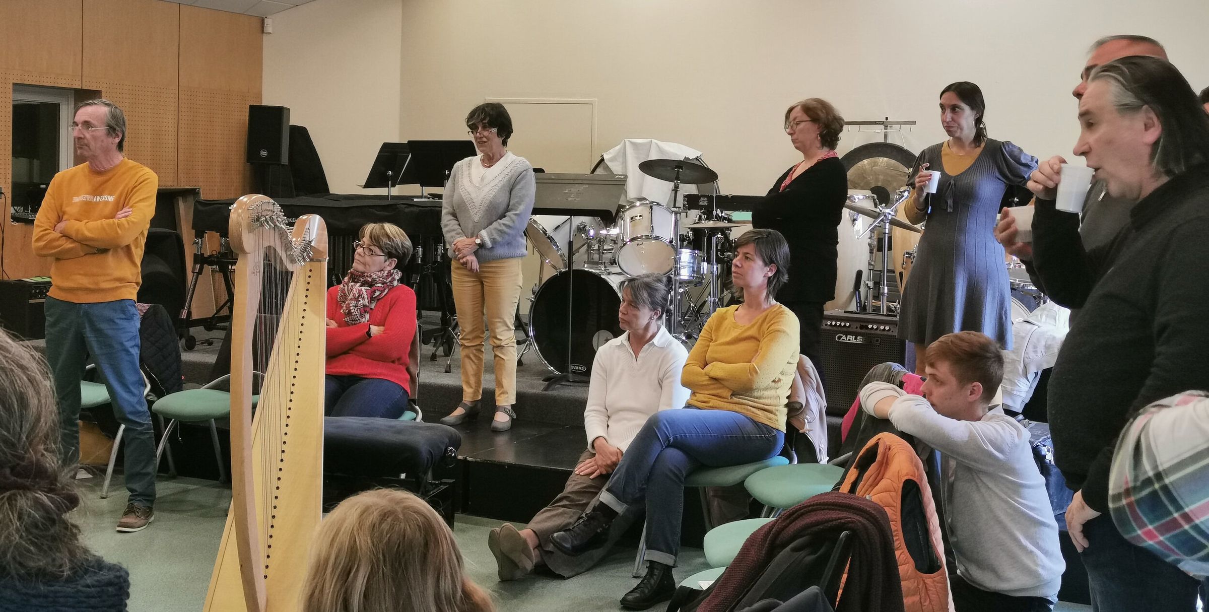 Atelier en salle de répétition : une harpiste joue, les autres musiciens écoutent debout et assis.